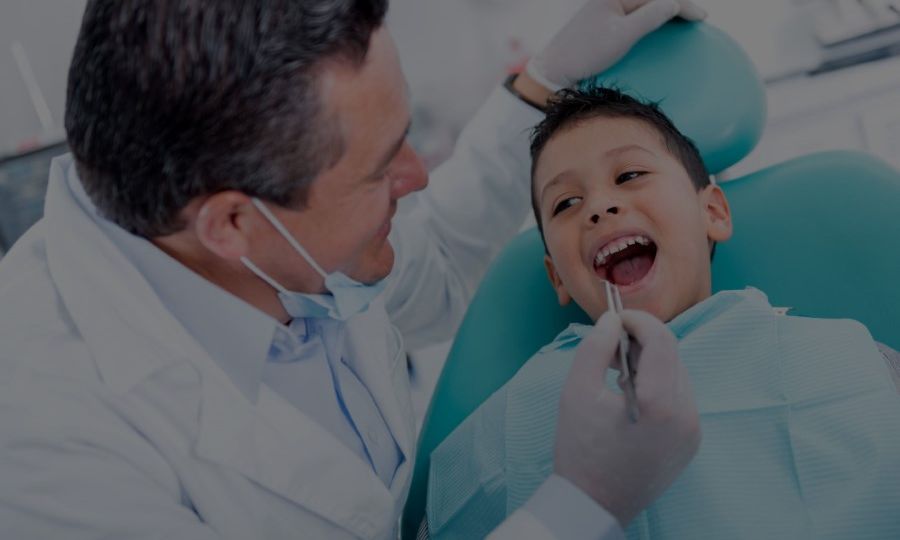 Young boy with mouth open getting teeth checked by pediatric dentist