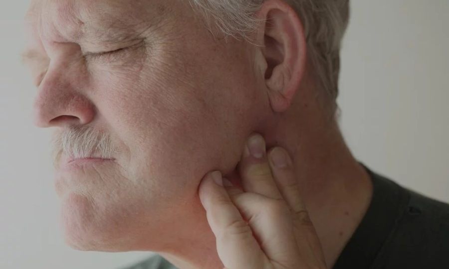 Man experiencing TMD pain holding jaw with left hand