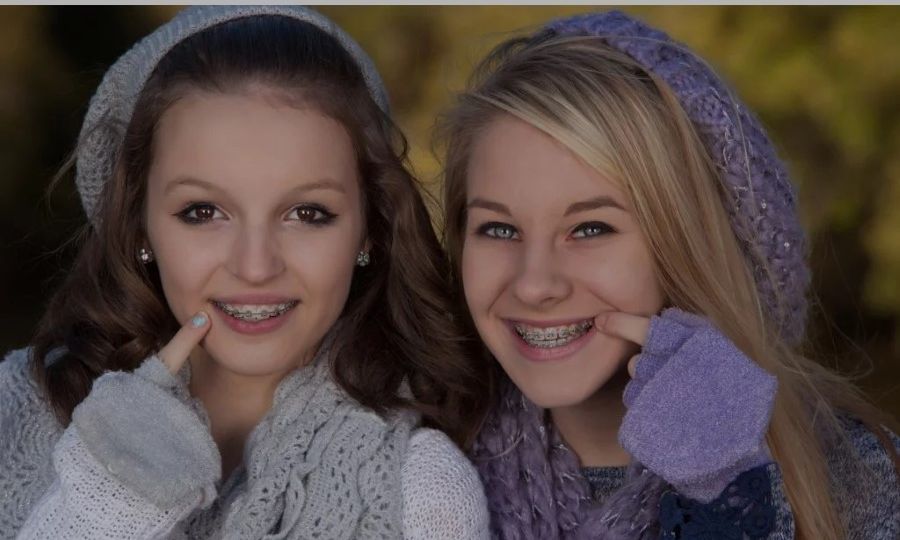Two teen girls with braces pointing towards their mouths