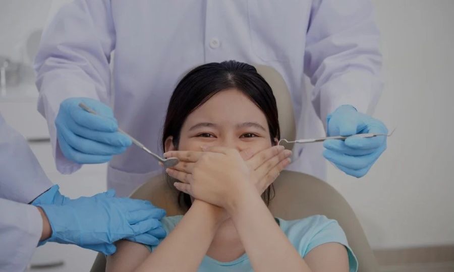Young girl covering mouth with both hands while getting dental treatment