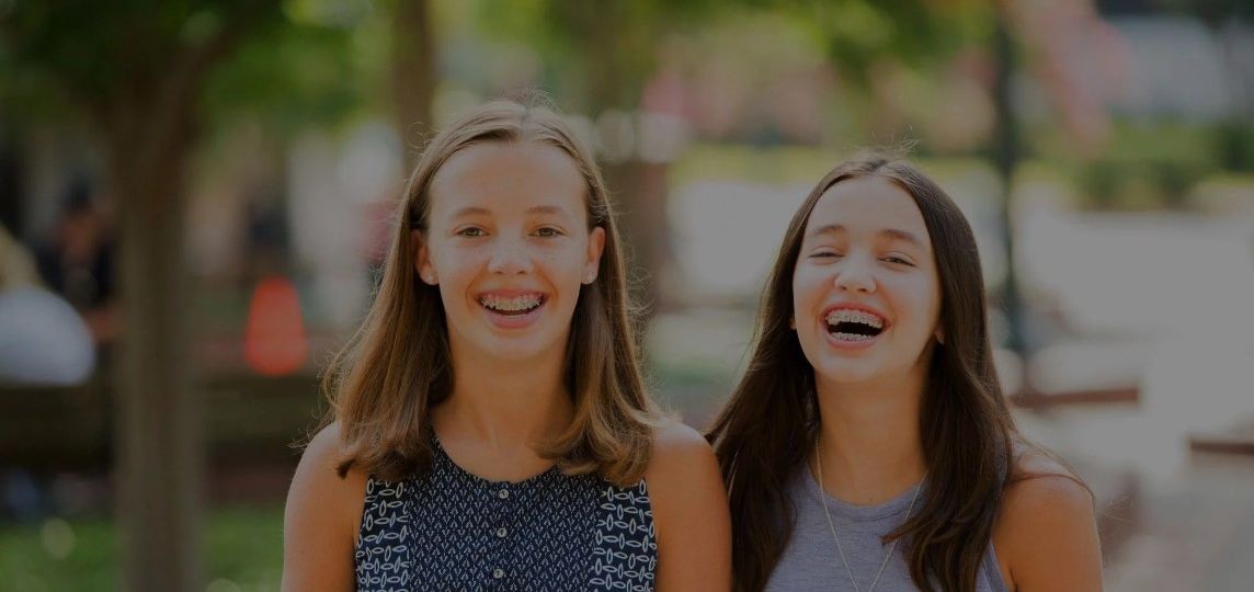 Two teen girls with braces laughing while out in the park