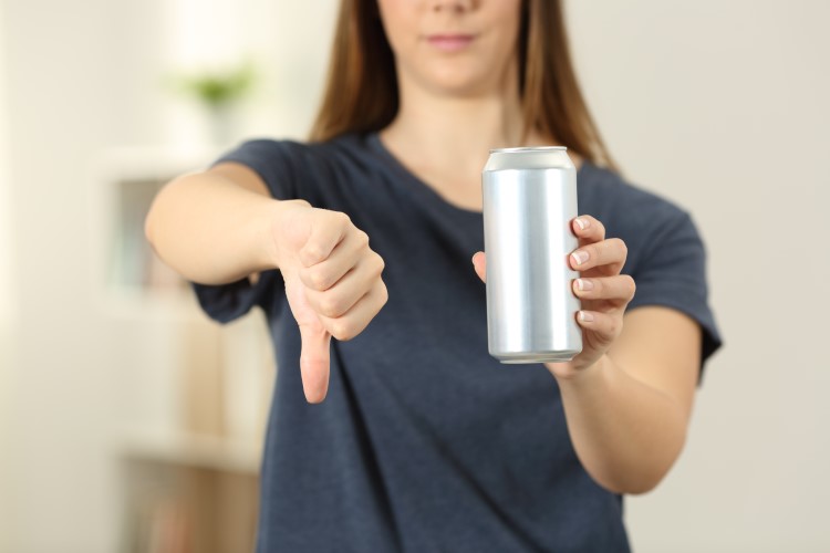 Front view close up of a woman hands holding a soda drink can with thumbs down at home