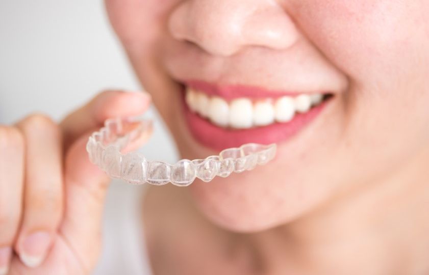 A smiling woman holding an invisalign braces or invisible retainer, orthodontic equipment
