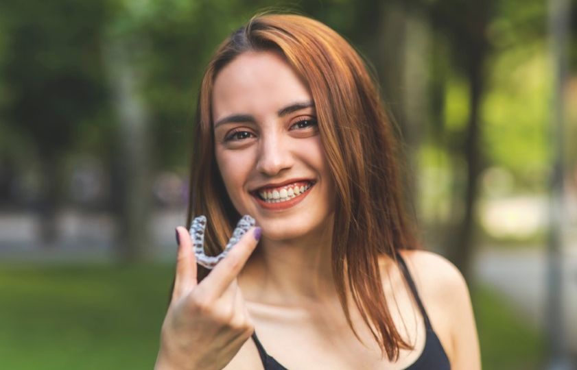 smiling Turkish woman is holding an invisalign bracer with vibrant colors