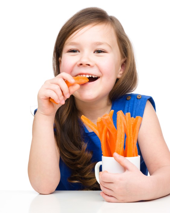 Little girl smiling while eating fresh carrot sticks
